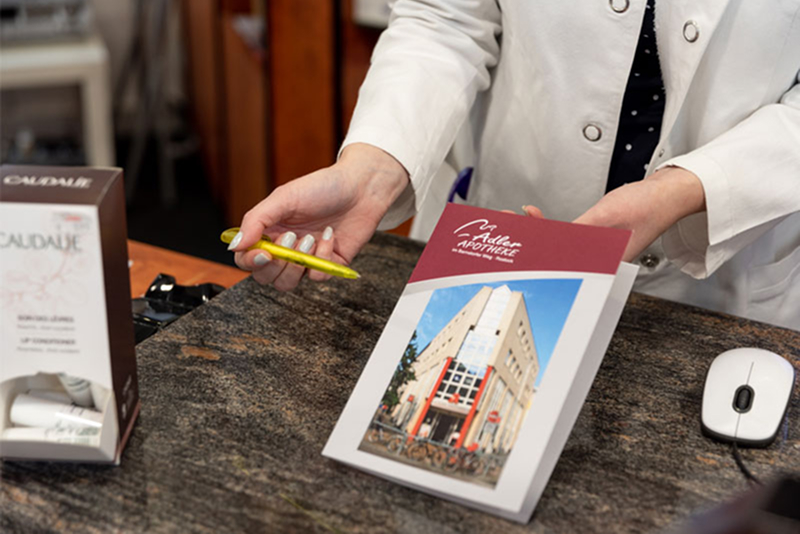 Apothekerin zeigt Informationsflyer der Adler Apotheke am Beratungstresen.